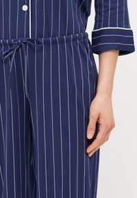 Conjunto de pijama azul-marinho com riscas brancas verticais, apresentando um corte descontraído, cintura elástica e uma parte de cima abotoada com mangas com punhos.
