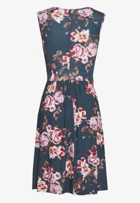 Robe sans manches de longueur genou avec un fond bleu foncé et un motif floral rose, blanc et marron, vue de dos avec une taille froncée et des plis.