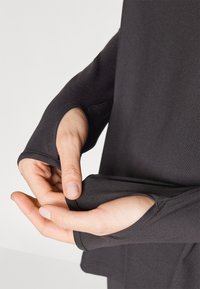 Black long-sleeve top with thumbholes in the cuffs. Fabric appears smooth and stretchy, featuring a fitted design.