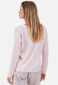 Hellrosa kabelgestrickter Pullover mit langen Ärmeln und lockerem Schnitt, mit gerippten Bündchen und Saum, der strukturierte Muster zeigt.