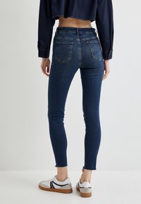 Jeans ajustados azules de cintura media, con dos bolsillos traseros, dobladillo deshilachado y combinados con zapatillas blancas.
