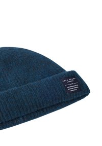 Knitted beanie in dark blue with a textured pattern. Features a visible brand label on the folded brim. Soft wool blend material.