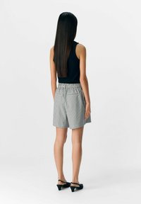 Sort ærmeløs top, hvide og grå stribede shorts med elastisk talje. Sorte hæle, glat tekstur og afslappet pasform.