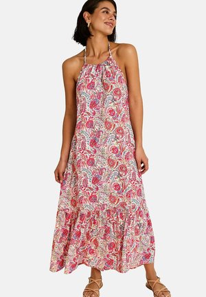 Femme portant une robe maxi sans manches à col licou avec un motif floral paisley rouge et rose, associée à des sandales beiges à brides.