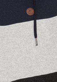 Grijze, marineblauwe en zwarte sweatshirt met een gestructureerde afwerking, voorzien van een ronde bruine leren patch en een zwarte koord met een metalen punt.