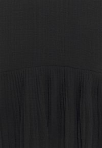 Svart klänning med en texturerad, krinklad tygkonstruktion, med en plisserad design i nederkant. Slät yta med lagerdetaljer.