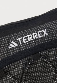 Musta reppu, jonka kangas on ruudullinen, valkoisella "TERREX"-logolla ja vastakkaisilla mustilla yksityiskohdilla, sekä säädettävät hihnat.