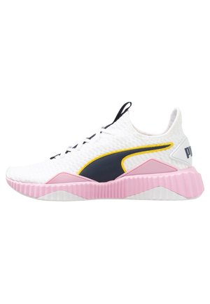 Chaussure de sport blanche avec dessus texturé, logo latéral noir et jaune, semelle rose côtelée et œillets noirs pour les lacets.