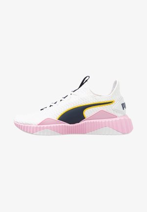 Chaussure de sport blanche avec dessus texturé, logo latéral noir et jaune, semelle rose côtelée et œillets noirs pour les lacets.
