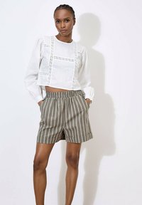 Witte cropped blouse met geborduurde details en lange pofmouwen, gecombineerd met groene gestreepte tailored shorts met een elastische tailleband.