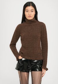 Barna bordázott garbó pulóver, puha, texturált anyagból készült. Hosszú ujjakkal rendelkezik, és enyhén cropped hemje van, logó részletekkel.