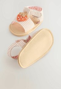 Pinkki ja valkoinen raitakuvioinen kangas, johon on brodattu mansikoita, avokärkiset sandaalit, joissa on tarranauha; varvaskohdassa on kohokuvioitu beige pohja.