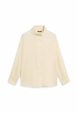 Blusa a manica lunga color crema con colletto alto e doppia fila di bottoni sul davanti, distesa su uno sfondo bianco.