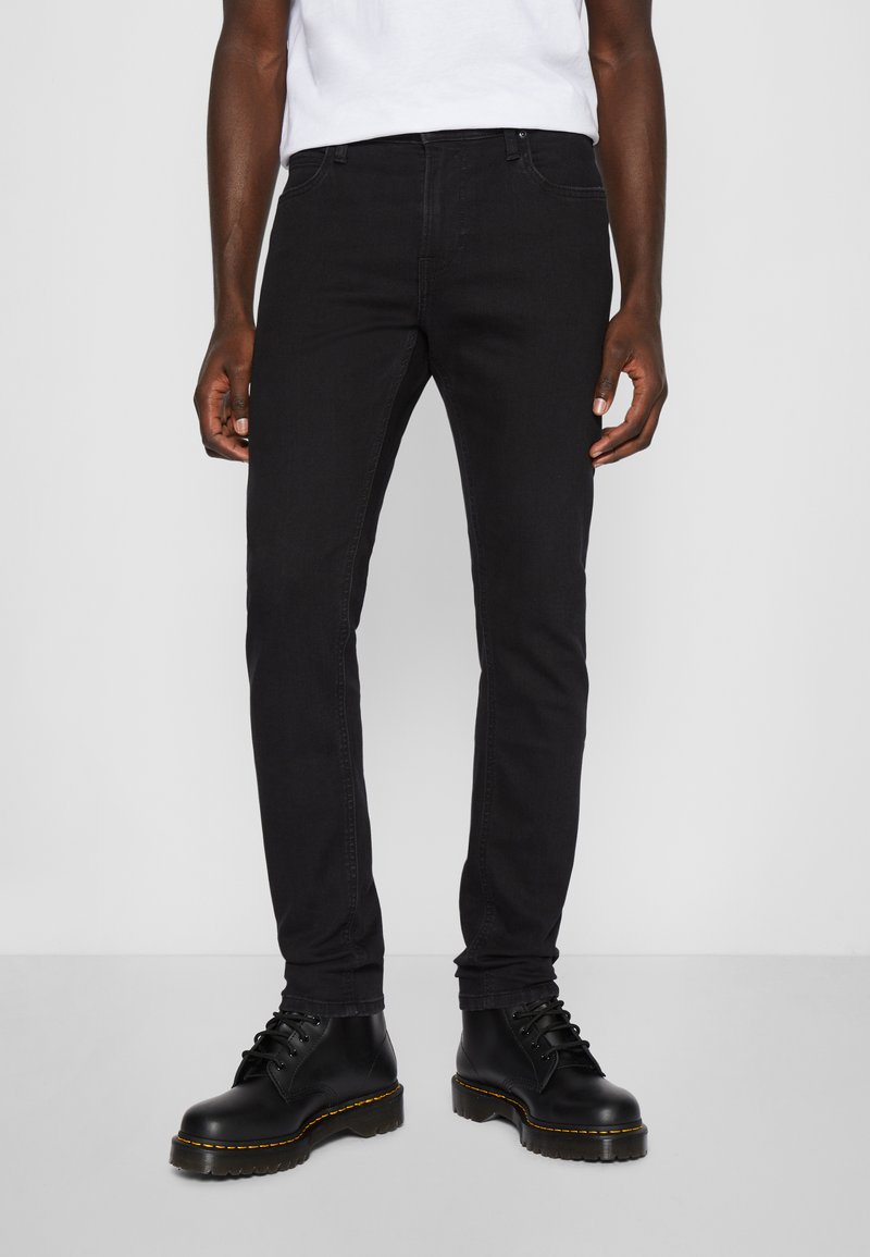 Black slim-fit jeans made of denim, featuring a classic five-pocket design and subtle stitching. Paired with black lace-up boots.