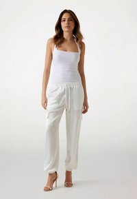 Débardeur blanc associé à un pantalon blanc ample avec des poignets élastiques et des poches, complété par des sandales à talons hauts couleur beige.