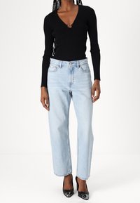 Top negro de manga larga acanalado con escote en V y detalle recortado, combinado con jeans de pierna recta azul claro y tacones de punta negra.