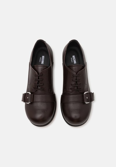 Brown leather shoes with a smooth texture, rounded toe, lace-up front, and a single strap with a metal buckle accent.