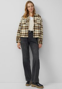 Koszulka z wełny w kratę w kolorach kremowym, brązowym i czarnym, w połączeniu z beżowym swetrem i czarnymi jeansami z wysokim stanem. Grube czarne buty na platformie.