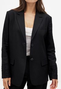 Schwarzer Blazer mit glatter Textur, zwei Knöpfen und einer einzelnen Brusttasche. Verfügt über gestickte Spitzenverzierungen an den Manschetten.