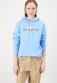 Šviesiai mėlyna kapucha su priekinėmis kišenėmis ir širdies piešiniu, kurioje parašyta "NEW YORK" rožinės ir juodos spalvos tekstu. Derinama su smėlio spalvos džinsais.