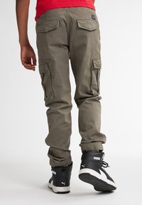 Olijfgroen katoen cargo pants, met zijzakken en een taps toelopende pasvorm. Gecombineerd met zwarte hoge sneakers met witte accenten.