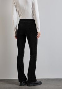 Pantaloni neri a coste e svasati realizzati in tessuto testurizzato, dotati di una vita alta. Indossati con una maglietta bianca a maniche lunghe.
