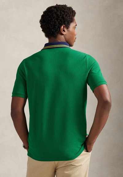 Πράσινο κοντομάνικο πόλο με σκούρο μπλε γιακά και κίτρινες λεπτομέρειες. Το ύφασμα έχει απαλή υφή και το σχέδιο είναι εφαρμοστό.