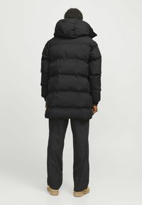 Pufferen jakke i ensfarvet sort med en stor hætte, der har et quiltet design og en afslappet pasform, parret med cargo bukser og brune støvler.