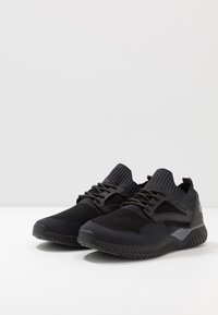 Scarpe sportive nere con una tomaia in mesh traspirante, dettagli testurizzati, colletto imbottito e design con lacci. Presentano suola in gomma e un branding discreto.