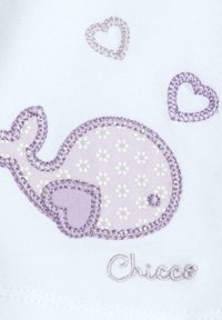 La tela blanca presenta una ballena morada bordada con patrones florales, acentuada por pequeños corazones morados y el nombre "Chicco" debajo.