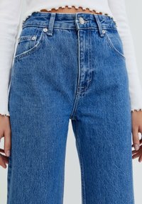 Jeans de mezclilla azul de cintura alta con un ajuste ligeramente suelto, que presentan un ligero desgaste, detalles de costura y un cierre de botón clásico.