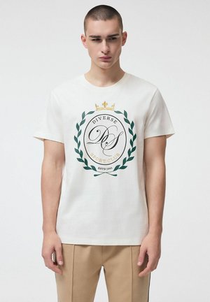 Młody mężczyzna z krótkimi włosami w białej koszulce z zielonym wieńcem laurowym, złotą koroną i napisem "Diverse Sport Club".