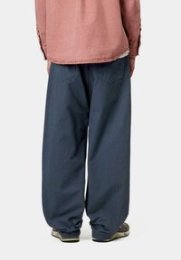Pantalones sueltos de un azul marino oscuro con un puño en el tobillo, combinados con una camiseta de manga larga de color rosa claro. Los bolsillos traseros son visibles.