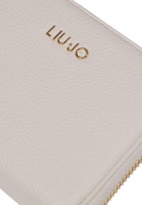 Portafoglio in pelle beige chiaro con superficie texturizzata, logo dorato "LIU.JO" e chiusura con zip arricchita da dettagli in oro.