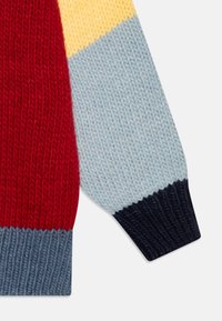 Strikkegenser med ermer i seksjoner av rød, gul, lyseblå og mørkeblå. Teksturert mønster med ribbede mansjetter. Mykt garnmateriale.