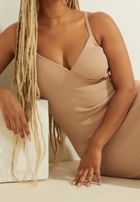 Abito bodycon a coste nudo con sp thin, caratterizzato da una scollatura a V. Un blocco geometrico bianco è parzialmente visibile. Tessuto testurizzato e tonalità della pelle liscia.