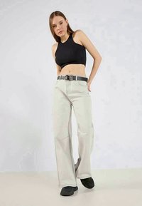 Light grey wide-leg pants made of cotton, featuring a black belt with a silver buckle. Worn with a fitted black crop top and black shoes.