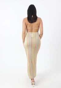 Sukienka maxi z dekoltem halter, przylegająca do ciała, wykonana z metalicznego materiału w pionowe pastelowe paski. Otwarty tył i długość do kostek. Gładka tekstura.