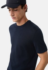 Dunkelblauer Kurzarmpullover mit geripptem Rundhalsausschnitt, glatter Textur und tailliertem Schnitt. Getragen mit einer passenden blauen Mütze.
