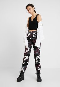 Kamuflasjonsbukser i burgunder, svart og hvit med elastisk kant, kombinert med en svart ribbet crop top og en hvit oversized jakke.