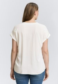 Vit kortärmad blus med rullade ärmar, rund halsringning och lös passform. Slät textur, lättviktsmaterial och rundad nederkant.