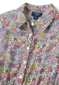 Camicia floreale multicolore con colletto corto e apertura con bottoni. Presenta fiori rosa, gialli e verdi con un motivo di testo giocoso su un tessuto leggero.