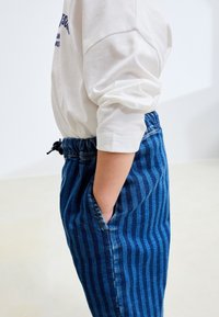 Blå randiga denimbyxor med elastisk midja, utrustade med sidofickor och snöre för justering. Matchas med en vit långärmad tröja.