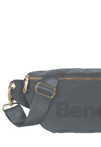 Grijze schoudertas van gestructureerde stof, met een gouden rits en hardwaren, een verstelbare schouderband en een opvallend gedrukt logo.