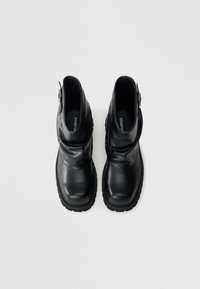 Mustad nahast pahkluu saapad kortsutatud disainiga, paksud kummist tallad ja külgmine pandlaga detail. Sile tekstuur ja ümar kanna kuju.