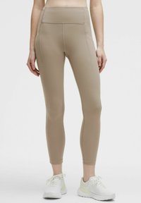 Beige högmidjade leggings i stretchmaterial, med sidofickor och en slät yta; tätsittande design med avsmalnande vrist.