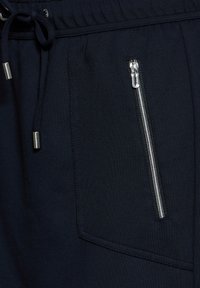 Pantalons navy avec taille élastique, dotés d'un cordon de serrage et d'une poche zippée sur le côté, fabriqués à partir d'un tissu texturé.