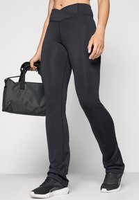 Black athletic leggings with a high waistband, smooth texture, and contrasting stitching, paired with a black gym bag and sports shoes.