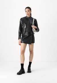 Giacca in finta pelle nera con chiusura a bottoni, gonna abbinata, maglia a maniche lunghe texturizzata, calze nere e scarpe nere chunky. Accentata da una borsa argentata.