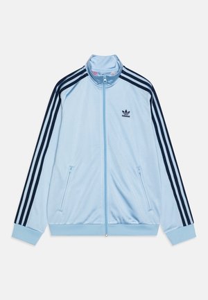 Jasnoniebieska kurtka sportowa Adidas zapinana na zamek, z czarnym wzorem trzech pasków na rękawach oraz logo Adidas na lewej piersi.